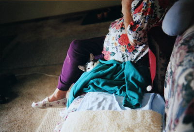 Low section of woman sitting on sofa with cat in home