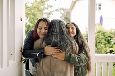 Rear view of senior woman embracing smiling daughter and granddaughter at entrance of house