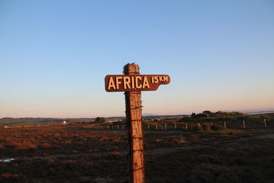 Close-up of road sign on field against clear sky