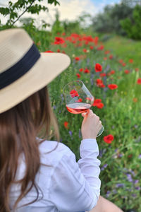 Rear view of woman holding red flowering plants on field