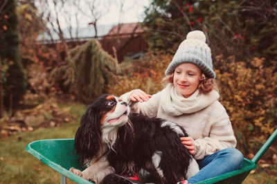 Girl sitting with dog in wheelbarrow on field