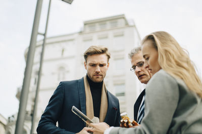 Low angle view of worried business executives looking at mobile phone while standing in city