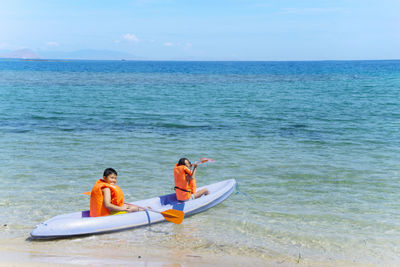 Friends kayaking on sea against sky