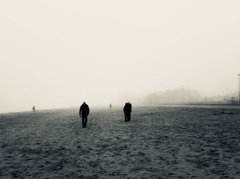 Rear view of silhouette people walking on sea during winter