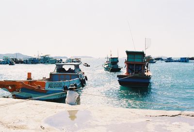 Boats moored at harbor against clear sky