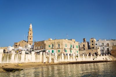 Buildings by river against clear blue sky