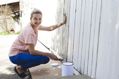Portrait of smiling woman painting wooden wall