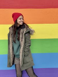 Portrait of young woman standing against rainbow wall