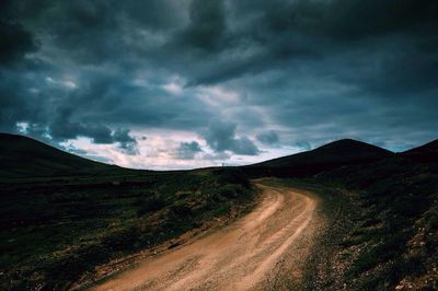 Road passing through landscape against cloudy sky