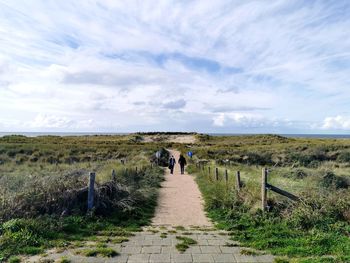 Rear view of people walking on landscape against sky