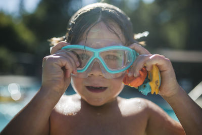 Portrait of shirtless boy adjusting swimming goggles at poolside