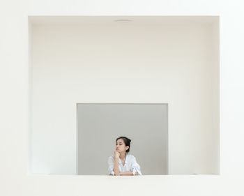 Portrait of a young woman standing against white wall