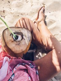 Low section of woman with coconut sitting at beach