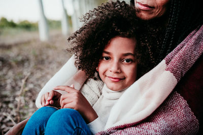 Portrait of smiling daughter sitting with mother on land