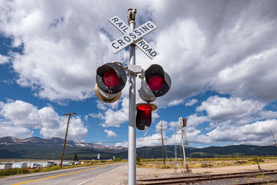 Railroad crossing sign against rocky mountains and cloud-sky in colorado, usa