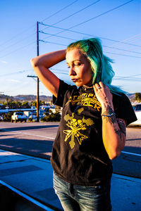 Young woman standing by car on road against clear blue sky