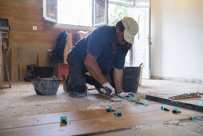 Mature man laying cement on parquet floor in house