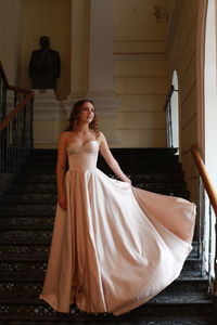 Smiling beautiful young woman wearing dress while standing on staircase