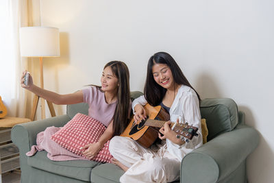 Portrait of young woman playing guitar while sitting on sofa at home