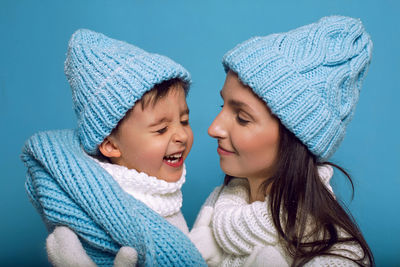 Mother and son in white sweaters and blue hats stand on a blue background in the studio