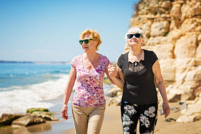 Two elderly women are walking along the rocky shore