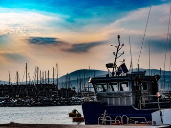 Sailboats moored at harbor against sky during sunset