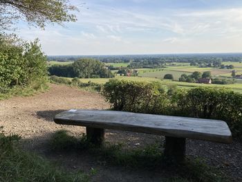 Bench on field by trees against sky