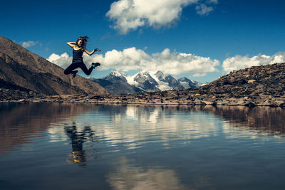 Man jumping over lake against sky