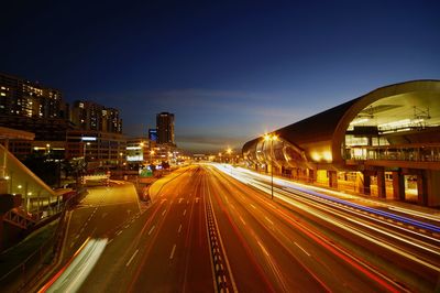 Light trails on road amidst buildings against sky at night