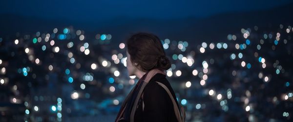 Rear view of woman standing in illuminated city at night