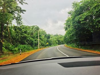 Road amidst trees against sky seen through car windshield