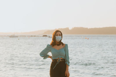 Young woman standing at beach against sky