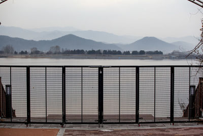 Railing by lake against mountains during foggy weather