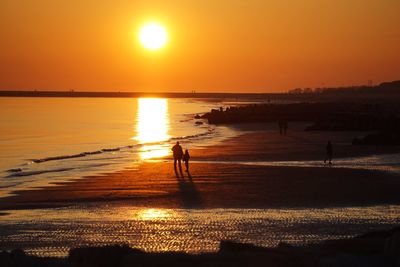 Silhouette people on beach against orange sky