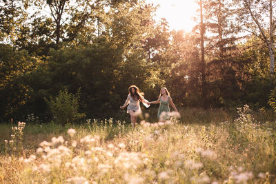 Happy lesbian couple holding hands while running in forest in summer