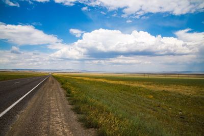 Empty road amidst field against sky