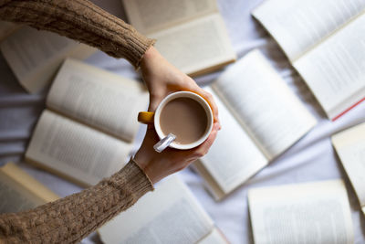 Hand picking up a cup of warm coffee with books.