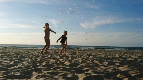 Full length of girls playing at beach against sky