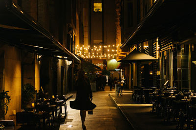 People walking on illuminated street amidst buildings at night
