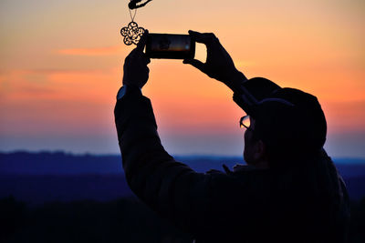 Man photographing sky through mobile phone during sunset