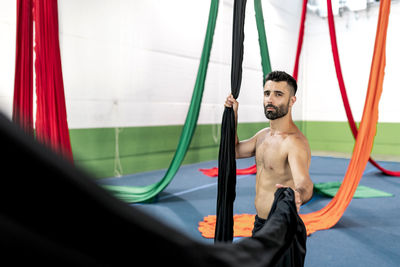 Crop muscular man grasping piece of black aerial silk during dance rehearsal in modern studio