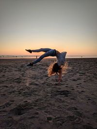 Woman jumping at beach against sky during sunset