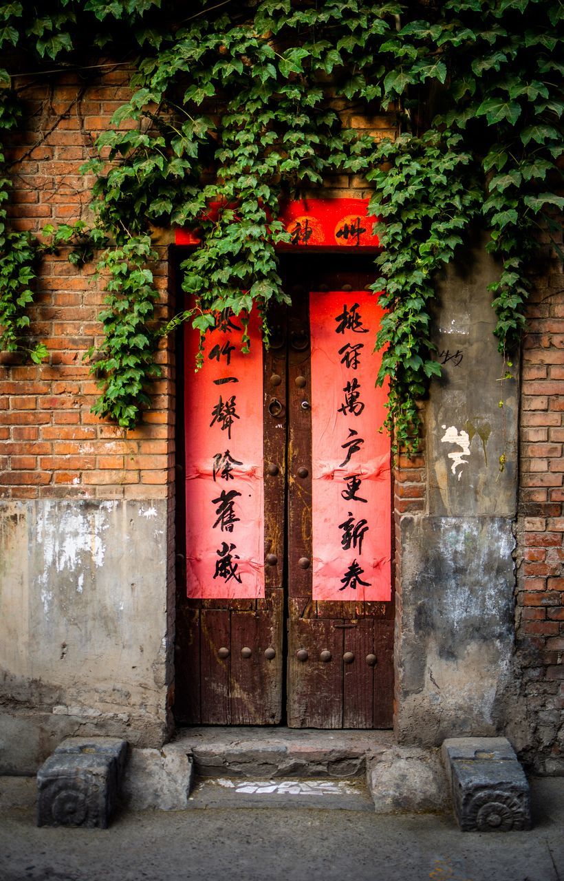 architecture, text, built structure, communication, non-western script, no people, wall, script, wall - building feature, day, building, entrance, building exterior, door, plant, nature, outdoors, brick, stone wall, message