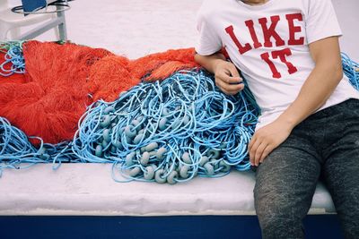 Midsection of man sitting by fishing net on boat