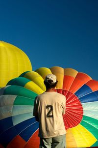 Rear view of man with balloons against clear blue sky