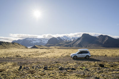 Car driving on gravel road with mountains behind, in iceland