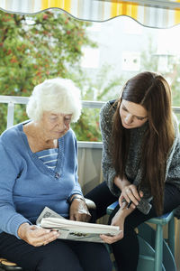 Grandmother and granddaughter reading newspaper on porch