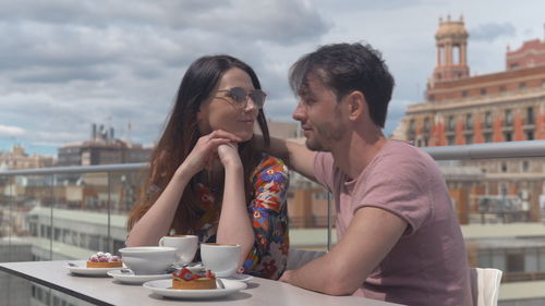 Young couple sitting at restaurant against city buildings