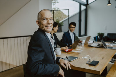 Portrait of businessman while male and female colleagues working in background at office