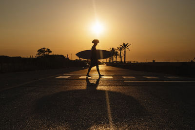 Silhouette of a surfer with afro hair walking at sunrise with surfboard